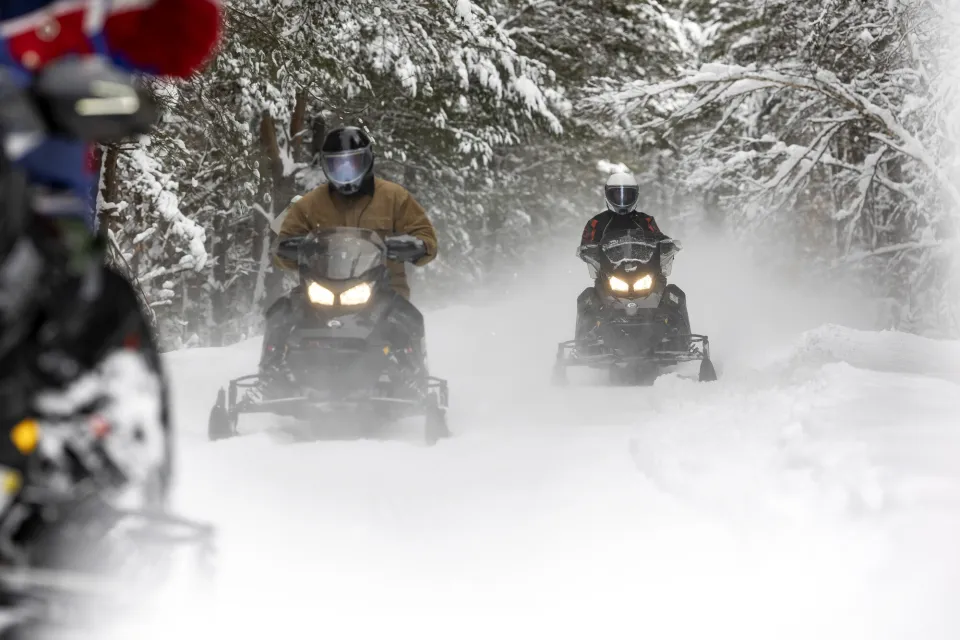 Three snowmobilers riding on a groomed trail.